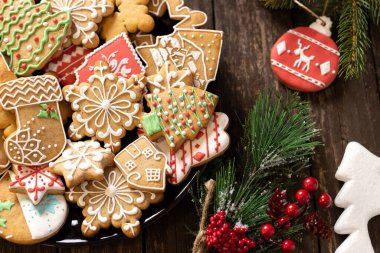 Tabakta çeşitli şenlik şekilli Noel kurabiyeleri, kozalak dallarının yanında, sade ahşap arka plan kavramına yerleştirilmiş.