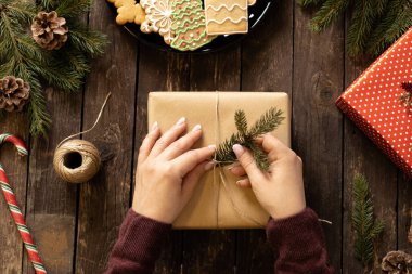 Noel hediyesini kozalakla süsleyen kadın ağaç masa arkaplan konseptinde her zaman yeşil olan bir dal.