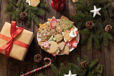 Noel ve Yeni Yıl temalı kırsal ahşap masa, paketlenmiş hediye kutusu, şeker kaplı kış tatili motifi ev yapımı zencefilli kurabiye ve bisküvi, şeker kamışı, yemyeşil dallar, tatil masası konsepti.