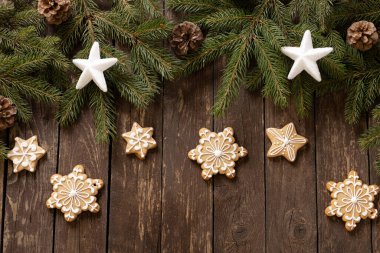 Yıldız ve kar tanesi şekilli zencefilli Noel kurabiyeleri kozalaklı kozalaklara ve ahşap arka plan konseptine yerleştirilmiş krema.