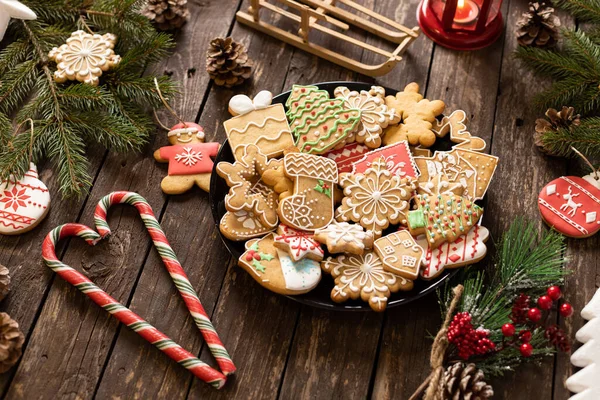 Geleneksel şekilli Noel kurabiyeleriyle dolu bir tabak şeker kaplı kış tatili temalarını Noel ve Yeni Yıl kavramları ile süslenmiş ahşap bir masaya koyun.  