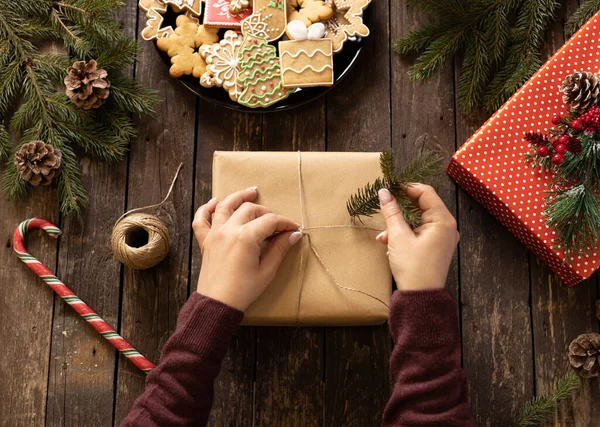 Noel hediyesini kozalaklı ağaç dallarıyla süsleyen bir kadının elleri bayram motifleri ve şekilleriyle süslü çerezlerle dolu, mutlu noeller konsepti.