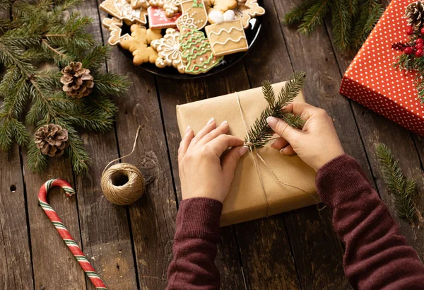 Noel hediyesini kozalakla süsleyen kadın ağaç masa arkaplan konseptinde her zaman yeşil olan bir dal.