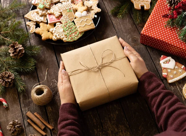Noel hediyesini, kış tatili şekilli kurabiyeler ve çeşitli süslemelerle süslenmiş ahşap bir masada tutuyorum. Mutlu Noeller konsepti.
