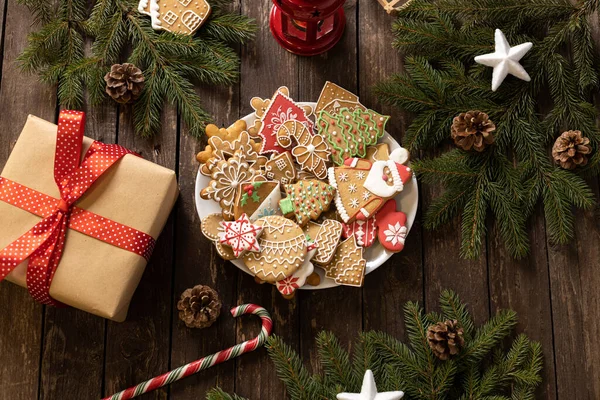 Noel ve Yeni Yıl temalı kırsal ahşap masa, paketlenmiş hediye kutusu, şeker kaplı kış tatili motifi ev yapımı zencefilli kurabiye ve bisküvi, şeker kamışı, yemyeşil dallar, tatil masası konsepti.