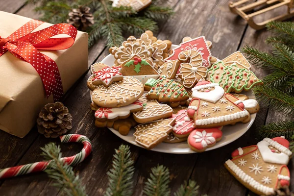 Noel hediyesi, lezzetli ev yapımı zencefilli kurabiye ve bisküvilerle dolu bir tabağın yanında güzelce hazırlanmış ve ahşap masa konseptine yerleştirilmiş şenlikli kış şekeri motifleriyle süslenmiş.