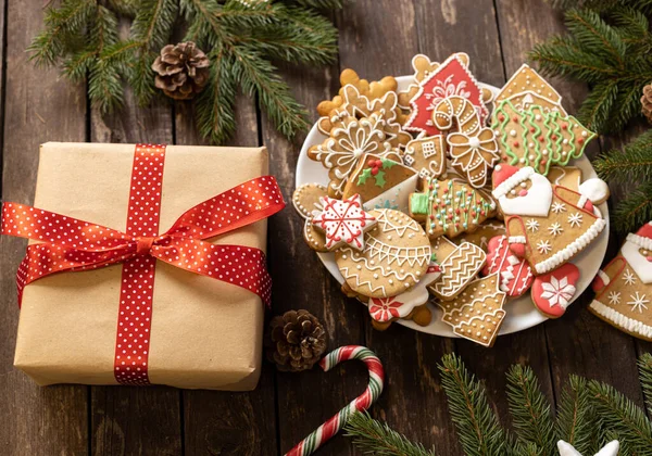 Noel hediyesi, lezzetli ev yapımı zencefilli kurabiye ve bisküvilerle dolu bir tabağın yanında güzelce hazırlanmış ve ahşap masa konseptine yerleştirilmiş şenlikli kış şekeri motifleriyle süslenmiş.