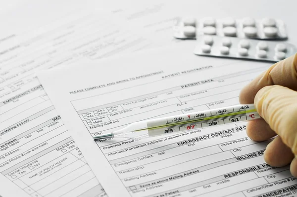 Thermometer in man hand on patient registration form — Stock Photo, Image