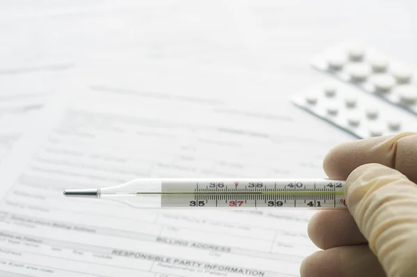 Thermometer in hand on patient registration form — Stock Photo, Image