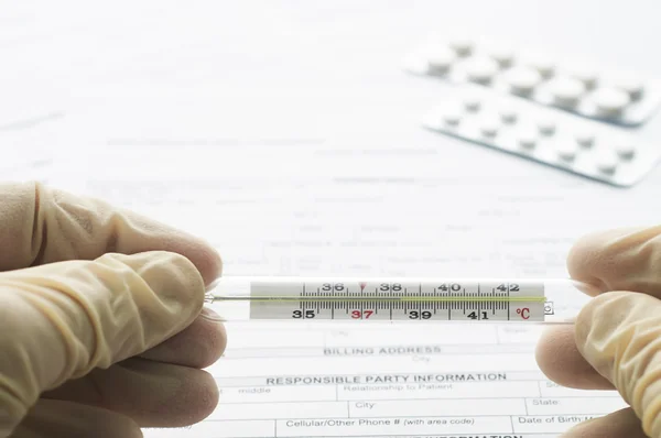 Thermometer in man hand on patient registration form — Stock Photo, Image