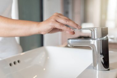 Kadın krom musluk lavabosunu kapat ve muslukta corona virüsü için ellerini sabunla ovala. Musluk ve su azalıyor. Lavabo lavabosu ve musluğu olan bir banyo. Musluk suyu..