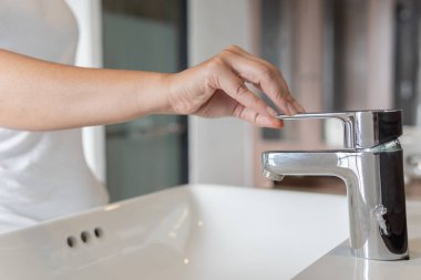 Kadın krom musluk lavabosunu kapat ve muslukta corona virüsü için ellerini sabunla ovala. Musluk ve su azalıyor. Lavabo lavabosu ve musluğu olan bir banyo. Musluk suyu..