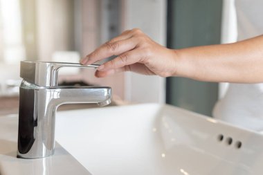 Kadın krom musluk lavabosunu kapat ve muslukta corona virüsü için ellerini sabunla ovala. Musluk ve su azalıyor. Lavabo lavabosu ve musluğu olan bir banyo. Musluk suyu..