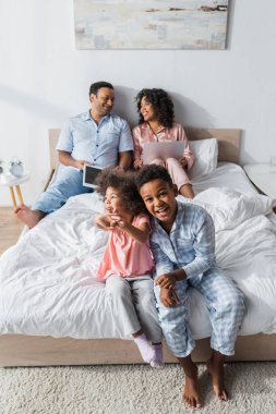 Mutlu Afro-Amerikan çocukları ellerinde aletlerle bulanık ebeveynlerinin yanında yatıyorlar.