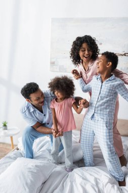 Neşeli Afro-Amerikan ailesi el ele tutuşup yatakta gülüyor.
