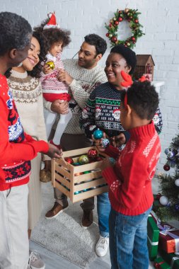 Neşeli Afro-Amerikan ailesi evdeki tahta kutudan noel balolarını seçiyor.