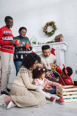 Afro-Amerikan ailesinin Noel balolarını seçtiği fincanlara bakan mutlu büyükanne ve büyükbaba.