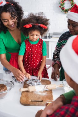 Ren geyiği boynuzları takan Afrikalı Amerikalı kız anne ve büyükanneyle yemek pişiriyor.