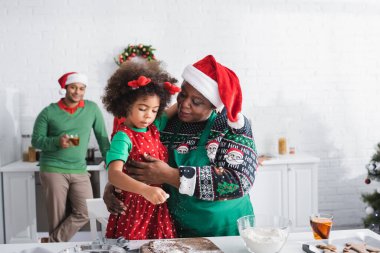 Afro-Amerikan kadın, mutfakta birlikte yemek yaparken torununa sarılıyor.