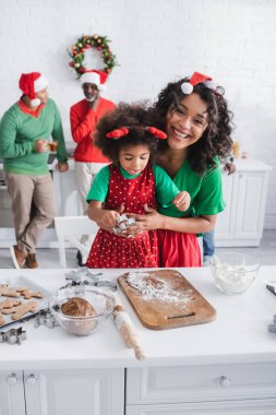 Neşeli Afrikalı Amerikalı kadın, kızını kucaklıyor ve Noel kurabiyeleri hazırlıyor. 