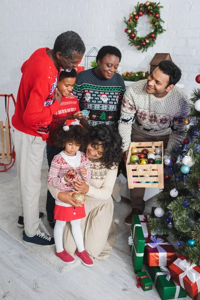 Mutlu Afrikalı Amerikalı adam elinde tahta bir kutuyla ailesinin yanında noel baloları tutuyor. 