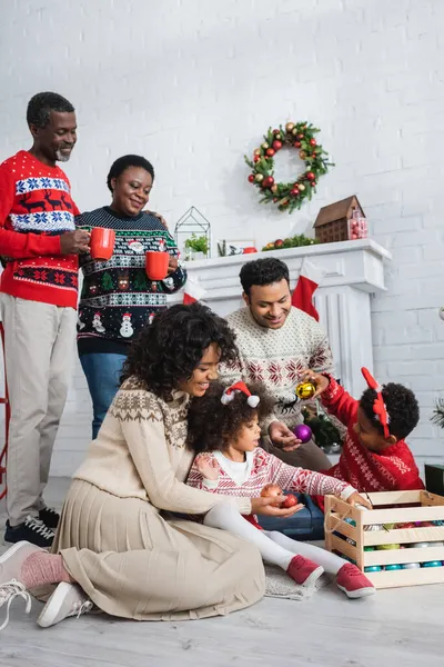 Abuelos Felices Con Copas Mirando Familia Afroamericana Elegir Bolas Navidad —  Fotos de Stock