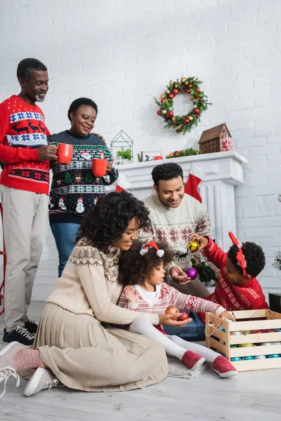 Afro-Amerikan ailesinin Noel balolarını seçtiği fincanlara bakan mutlu büyükanne ve büyükbaba.