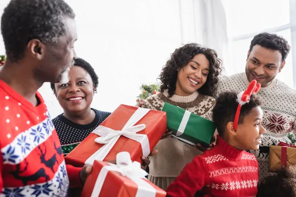 Mutlu Afro-Amerikan ailesi evde Noel hediyelerini tutarken gülümsüyor.