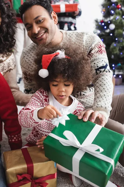 Noel Baba şapkalı Afrikalı Amerikalı kız Noel hediyeleri ve mutlu ebeveynler.