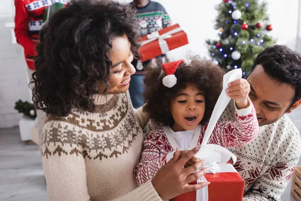 Asombrado Afroamericano Chica Apertura Navidad Presente Cerca Feliz Padres Borrosa — Foto de Stock