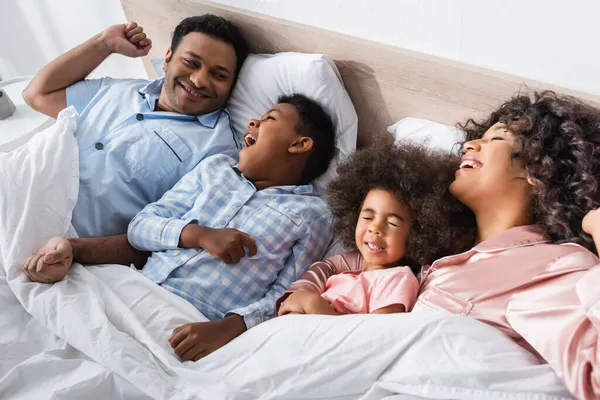 Niño Afroamericano Bostezando Mañana Mientras Yacía Cama Cerca Padres Felices —  Fotos de Stock