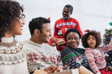 Afro-Amerikan ailesi oturma odasında konuşurken gülümsüyor.