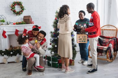 Afrikalı Amerikan ailesi Noel ağacının yanında süs eşyası seçiyor.