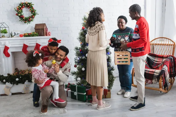 Afrikalı Amerikan ailesi Noel ağacının yanında süs eşyası seçiyor.