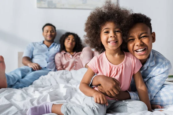 Vidám Afro Amerikai Fiú Átöleli Húgát Hálószobában Közelében Boldog Szülők — Stock Fotó
