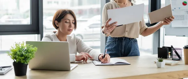 Mujer Negocios Escribiendo Cuaderno Cerca Del Ordenador Portátil Colega Afroamericano — Foto de Stock