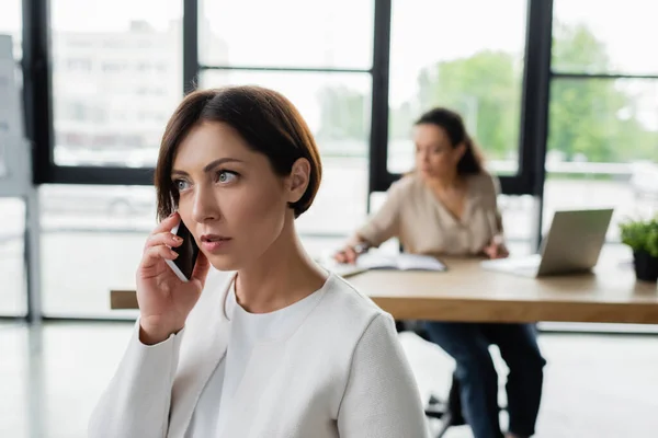 Businesswoman Rozmawia Przez Telefon Komórkowy Biurze Pobliżu Afrykańskiego Amerykańskiego Kolegi — Zdjęcie stockowe