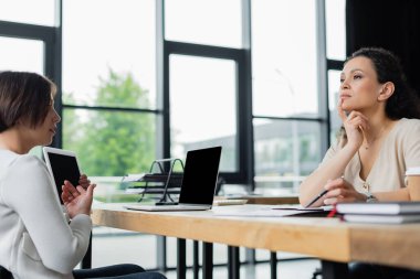 İş kadını, düşünceli Afrikalı Amerikalı meslektaşının yanında boş ekranla dijital tableti işaret ediyor.