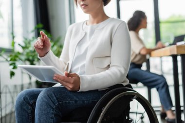 Ofiste dijital tabletle çalışırken tekerlekli sandalyedeki bulanık iş kadını parmağıyla işaret ediyor.