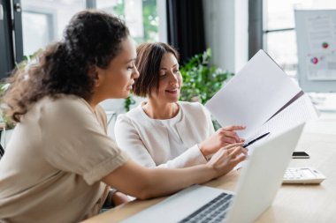 Irklar arası iş kadınları ofiste birlikte çalışırken belgeye işaret ediyorlar