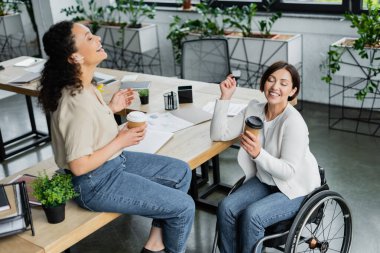 Heyecanlı Afrikalı Amerikalı iş kadını ve tekerlekli sandalyedeki meslektaşı kahve molasında gülüyorlar. 