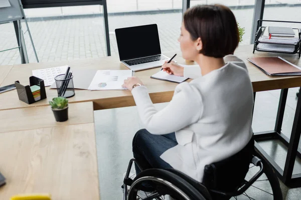 Verschwommene Geschäftsfrau Rollstuhl Schreibt Notizbuch Während Sie Mit Dokumenten Laptopnähe — Stockfoto