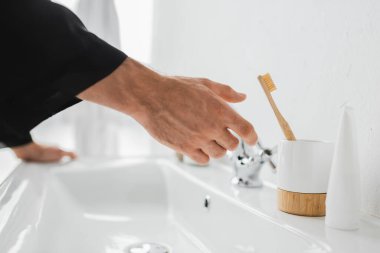 Banyoda lavabonun yanında elini diş fırçasına çeken adamın görüntüsü. 