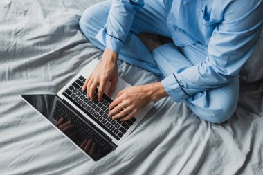 Yatağında boş ekranı olan dizüstü bilgisayar kullanan pijamalı genç bir serbest yazar. 