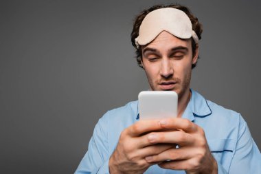 Gri renkte izole edilmiş akıllı telefon kullanan pijamalı uykulu adam. 