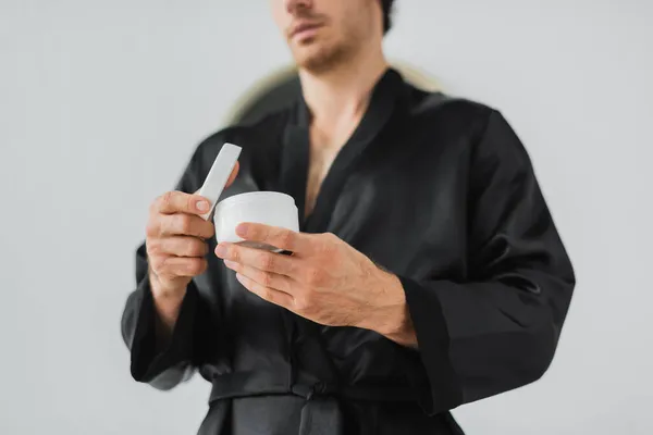 Cropped view of blurred man in robe holding cosmetic cream in bathroom