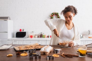Gülümseyen Afrikalı Amerikalı kadın mutfakta malzemeler ve Noel kurabiyeleri pişiriyor. 