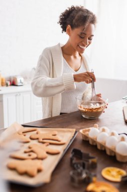Bulanık yumurta ve lezzetli noel kurabiyelerinin yanında yemek pişiren mutlu Afrikalı Amerikalı kadın. 