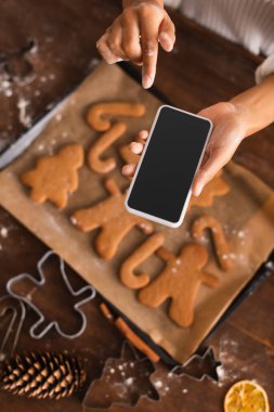 Ellerinde un olan Afro-Amerikan kadın, mutfakta bulanık noel kurabiyelerinin yanında akıllı telefon tutuyor. 