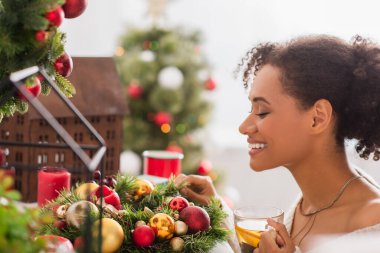 Gülümseyen Afrikalı Amerikalı bir kadının elinde bir fincan çayla Noel çelengi tutarken yan görünümü 